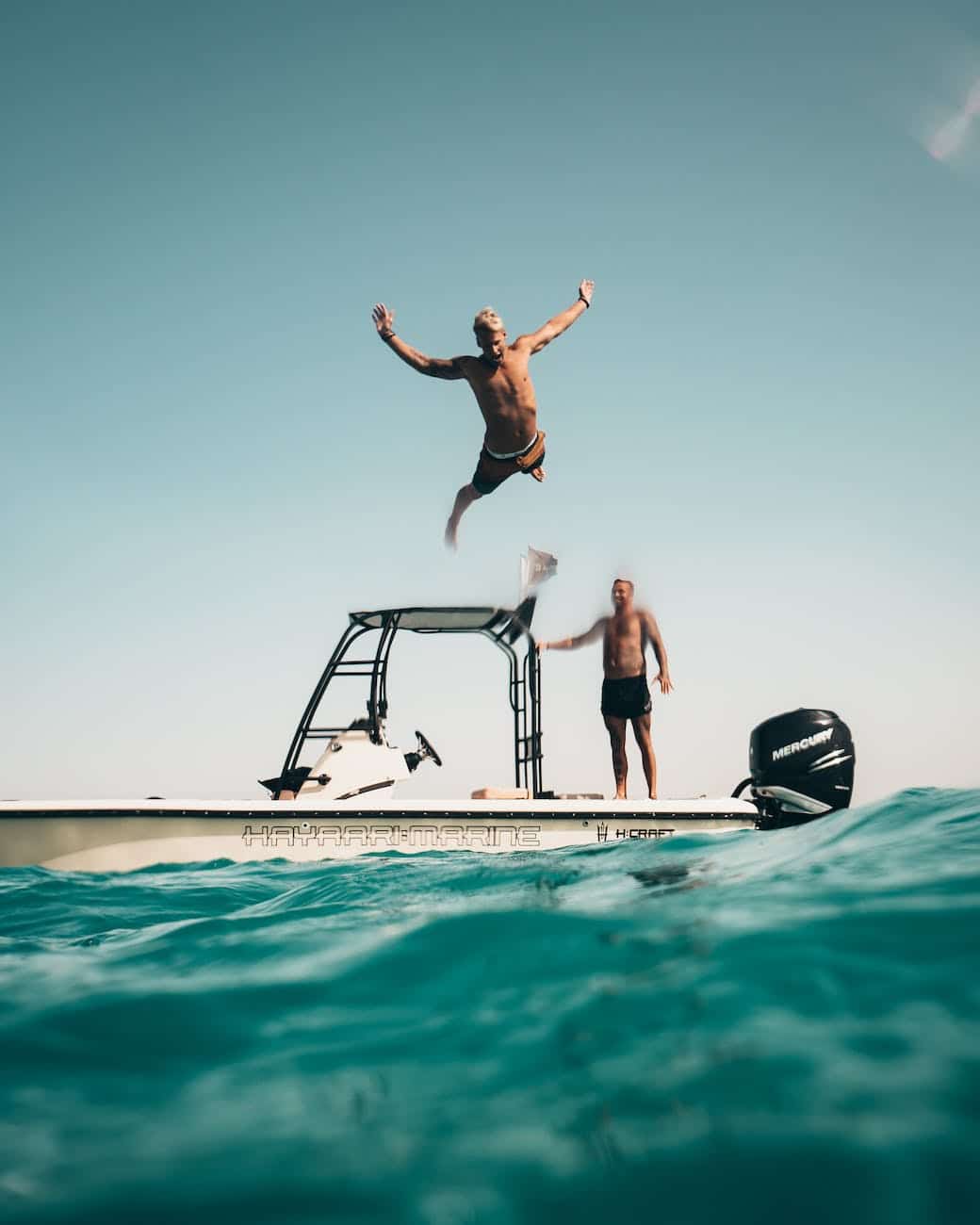 photo of man jumping from boat to the sea